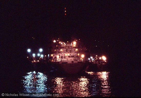 A large Russian mother ship takes on frozen fish and provides supplies to two of at least a dozen 300 ft. Soviet trawlers operating just outside the 12-mile limit off the California Coast on the night of July 3, 1976. In this end view a trawler can be seen on each side of the mother ship.