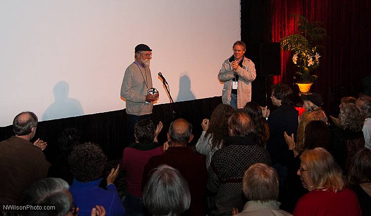 Les Blank holds the 2011 Maysles Award trophy as MFF advisor Jim McCullough and the audience applaud.