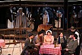 Mimi and Rodolfo join the group at Cafe Momus as the chorus of townspeople are seen outside (background).