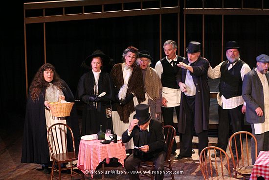 Townspeople (chorus) look on in amusement as Alcindora is stuck with the bill.