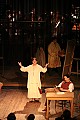 Narrator Lorry Lepaule sets the scene, back in the bohemian garret studio in Act IV of La Boheme. The orchestra can barely be seen in the background behind a scrim.